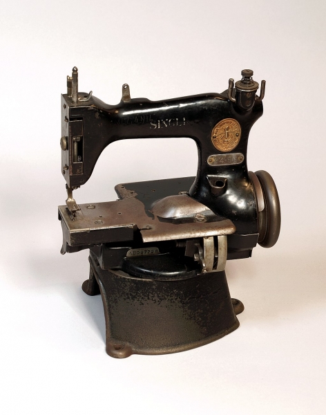 Handnaaimachine van gietijzer, deels zwart gelakt, model op hoge ronde voet “SINGER”, objectnr 64364. Museum Rotterdam via Wikimedia Commons, CC BY-SA 3.0