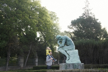 Man kijkt met kind op de schouders naar het beeld De Denker van Rodin