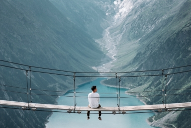 Man zit op hangbrug tussen twee bergen en kijkt naar een meer. Foto: Alex Azabache via Unsplash