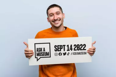 Persoon houdt een bord vast met daarop de tekst 'Ask a museum, sept 14 2022'