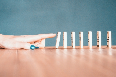 Hand met gelakte nagels tikt een rij dominosteentjes om. Foto: Bradyn Trollip via Unsplash