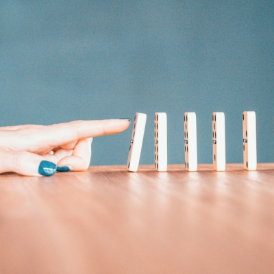 Hand met gelakte nagels tikt een rij dominosteentjes om. Foto: Bradyn Trollip via Unsplash